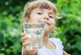 Glimlachend kind steekt een glas met water vooruit